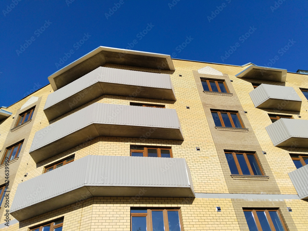 Obraz premium Facade of new multi-story residential building. Sale and rental apartments. Housing development. Cityscape. City life. Real estate. Blue sky. Mortgage concept. Condos. Interest Rate Increase. Flat.