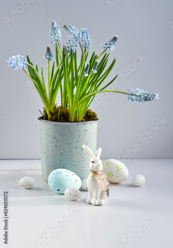 Easter composition with white rabbit, eggs and light blue muscari flowers in cup. Easter still life