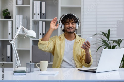 Young man enjoying music with headphones while working in modern office