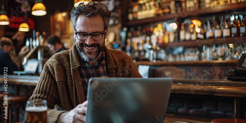 Joyful individual utilizing cellphone while multitasking on computer at a bar. photo