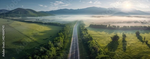 Aerial view of a straight country road through lush green fields and mountains in the background on a misty morning. photo
