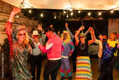 Friends in festive costumes dance and celebrate at an energetic outdoor party illuminated by string lights