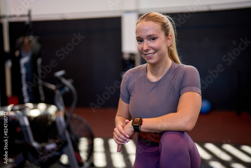 Athletic woman posing confidently in the gym as a personal trainer, surrounded by gym equipment, showcasing her professional and fit appearance.