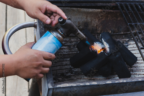 Man using BBQ lighter torch to start fire for charcoal.