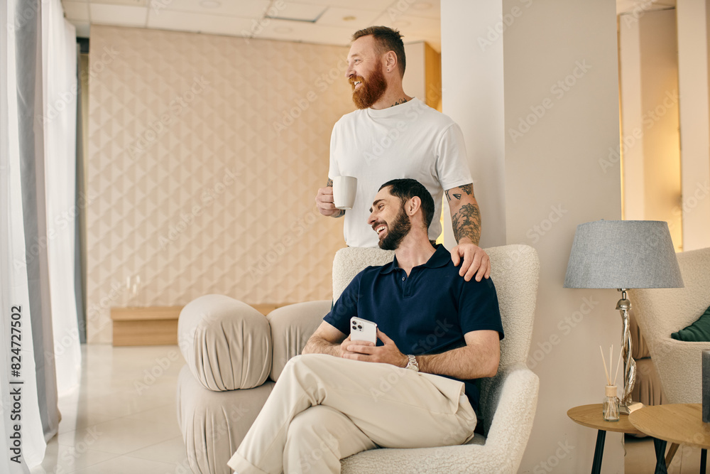 Two men, a happy gay couple, in casual clothes sit together on a chair in a modern living room, cherishing quality time spent. Two men, a happy gay couple, in casual clothes sit together on a chair in a modern living room, cherishing quality time spent.