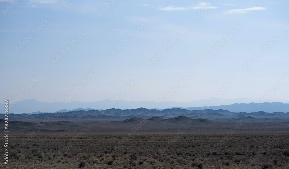 a vast desert landscape under a clear sky with layered mountain silhouettes receding into the distance, creating a serene and expansive view