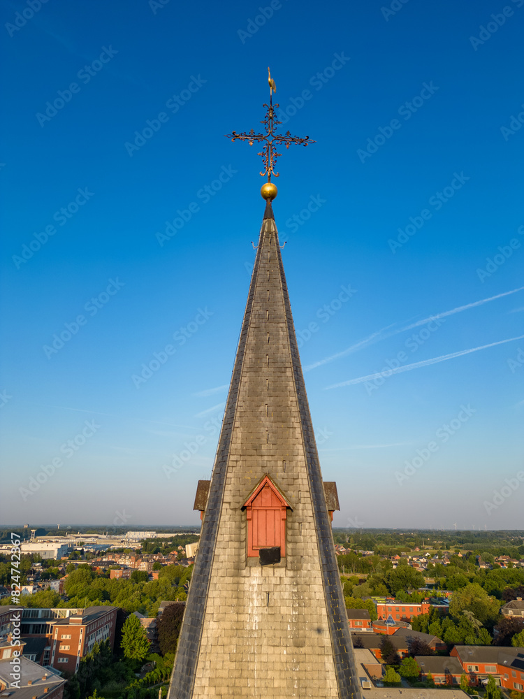 Fototapeta premium Aerial view of a church steeple with a cross in a suburban area, displaying architectural beauty under a clear blue sky