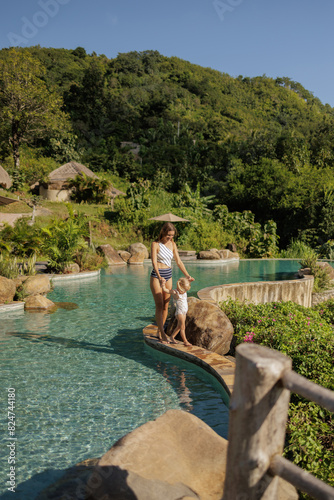 Mother and baby play in outdoor infinity swimming pool of luxury hotel resort in tropics. Happy family Mother with baby on the edge of  infinity pool. Happy child have fun on summer beach holiday