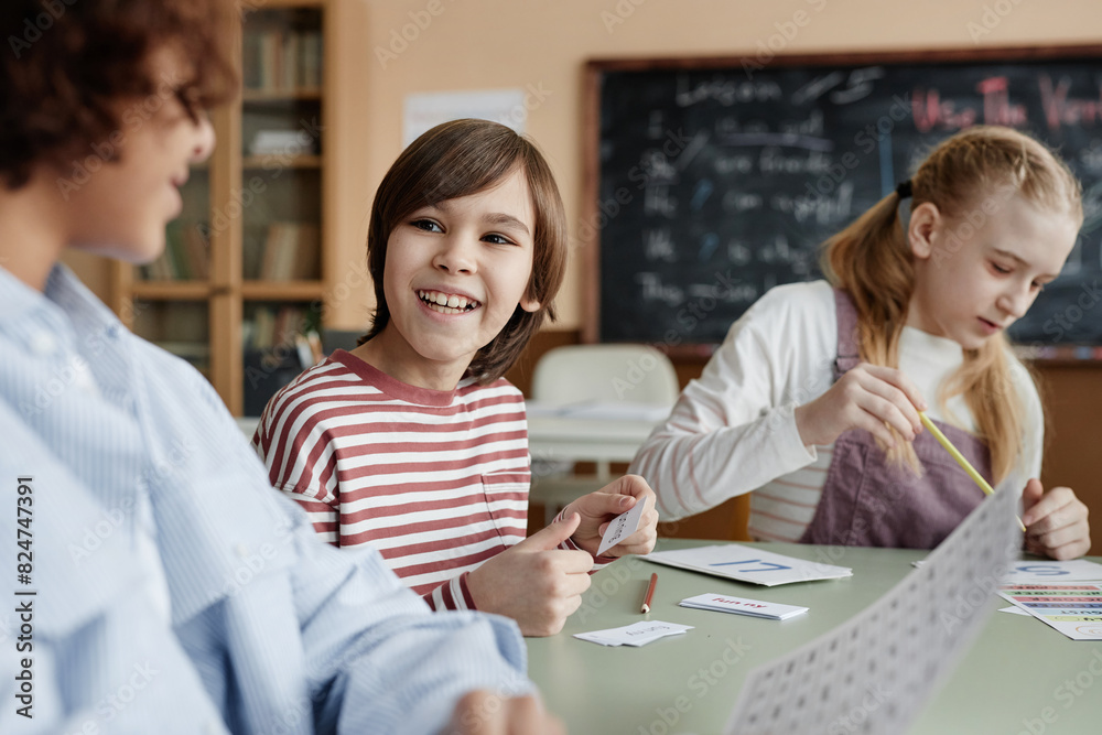 Cheerful Caucasian boy sitting at table in classroom chatting with his classmate during lesson Cheerful Caucasian boy sitting at table in classroom chatting with his classmate during lesson