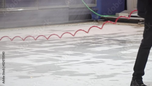 Man is spraying a floor with a water hose on ice rink freezing it.