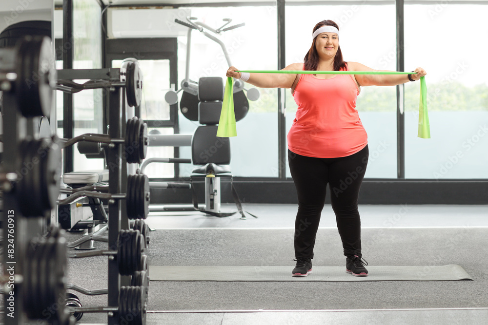 Fototapeta premium Corpulent woman standing on a mat and exercising with a rubber band
