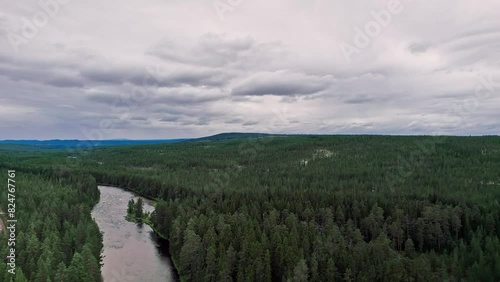 Drone ascends over the Storån River, revealing a breathtaking view of the lush forests and rolling hills of Idre, Dalarna, Sweden. photo