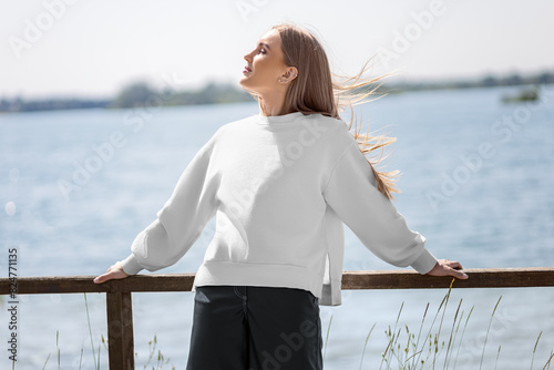 Mockup of a white sweatshirt on a blonde girl on the background of the river, quay, fashionable clothes, front view.
