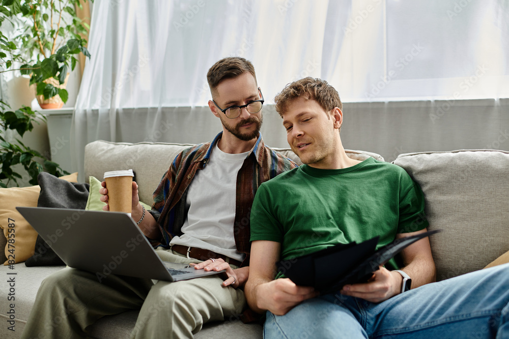 Two men in love sit on a couch, focused on a laptop, designing trendy attire in their workshop. Two men in love sit on a couch, focused on a laptop, designing trendy attire in their workshop.
