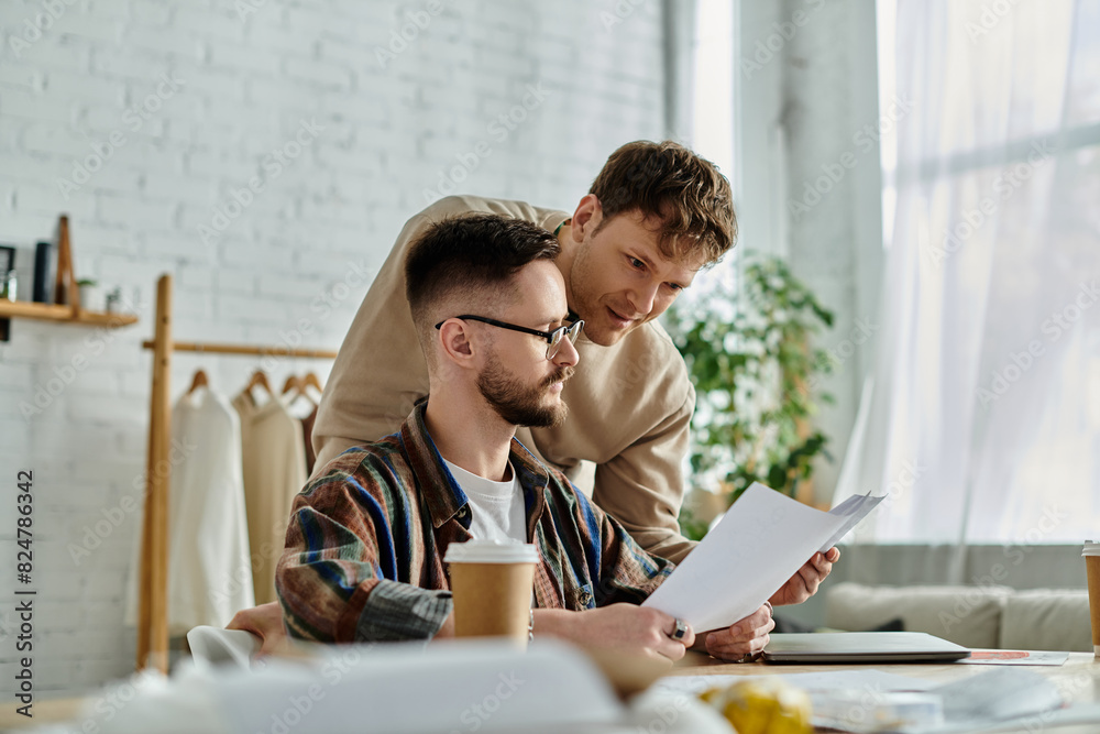 Two men in a workshop, engrossed in designing fashion pieces on a table. Two men in a workshop, engrossed in designing fashion pieces on a table.