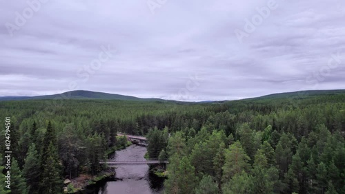 Drone rising above the treetops over a bridge with passing car to a stunning view of Storån river winding through the Swedish wilderness, with lush green forests and rolling hills in the background photo