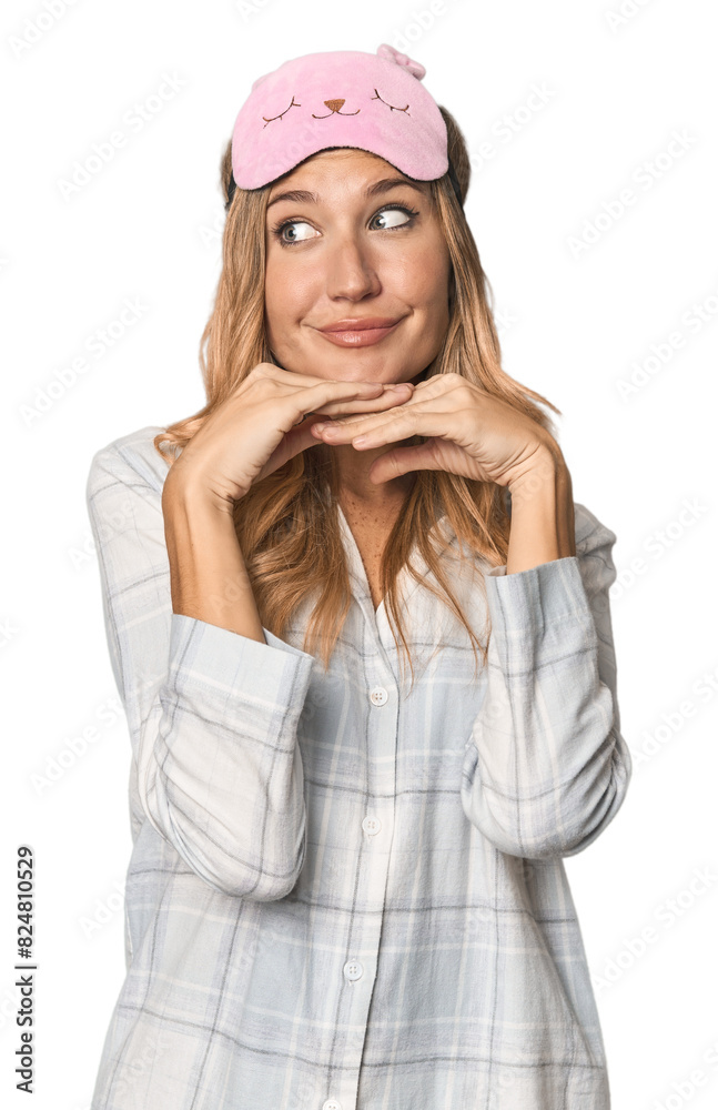 Blonde in pajamas with sleep mask keeps hands under chin, is looking happily aside. Blonde in pajamas with sleep mask keeps hands under chin, is looking happily aside.