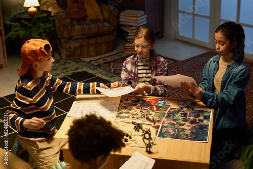 Tableau sur toile Four cute intercultural children sitting on the floor by table with boards, card
