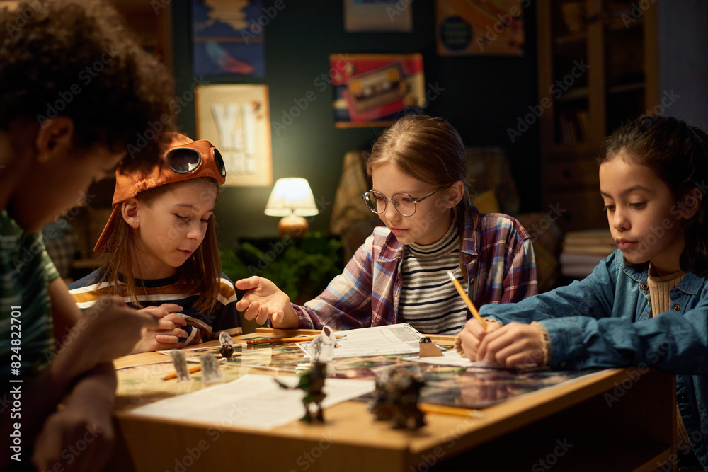 Fototapeta premium Several intercultural kids in casualwear reading rules of new tabletop game and choosing character roles before playing it together
