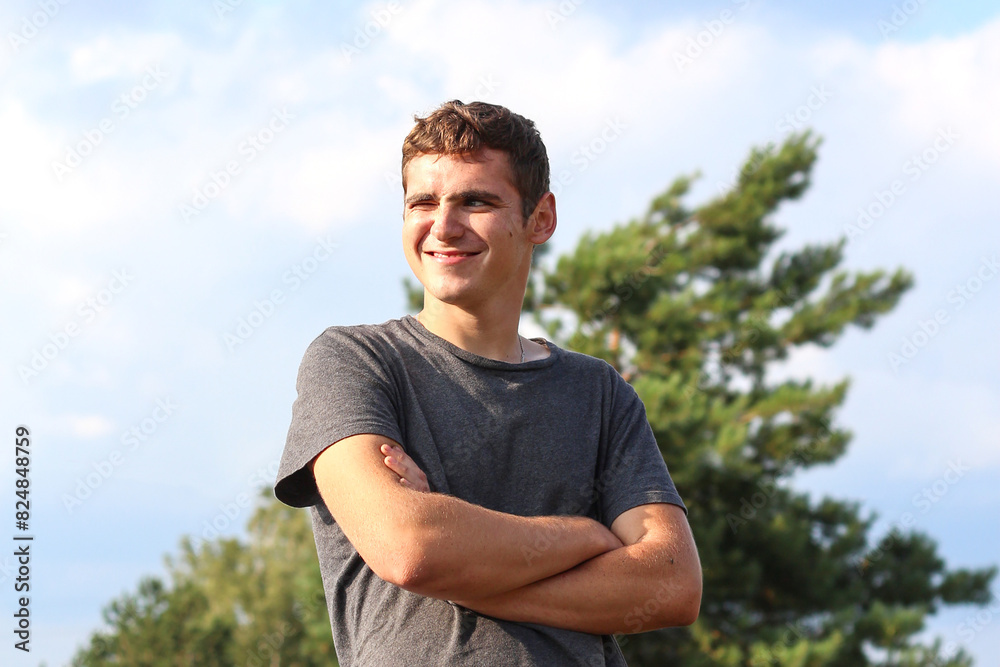 Young smiling man on the summer day. Happy and confident man with crossed arms. Candid young man outside. Nature blurred background Young smiling man on the summer day. Happy and confident man with crossed arms. Candid young man outside. Nature blurred background