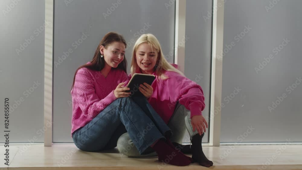 A two young girlfriends sitting on the floor and using tablet before math exam. Lesbians girls couple watching video together using tablet. Cute couple of female sitting together and doing homework A two young girlfriends sitting on the floor and using tablet before math exam. Lesbians girls couple watching video together using tablet. Cute couple of female sitting together and doing homework