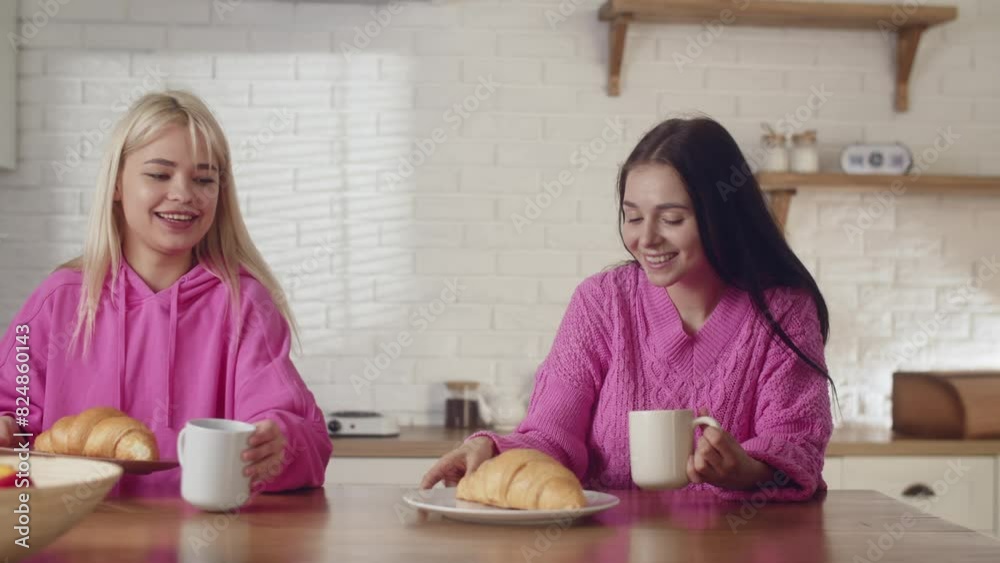 Holiday concept. Caucasian women couple having a lunch in kitchen. Eating french croissants at home. A young lesbians love joyful girlfriends staying home and eating french croissants Holiday concept. Caucasian women couple having a lunch in kitchen. Eating french croissants at home. A young lesbians love joyful girlfriends staying home and eating french croissants