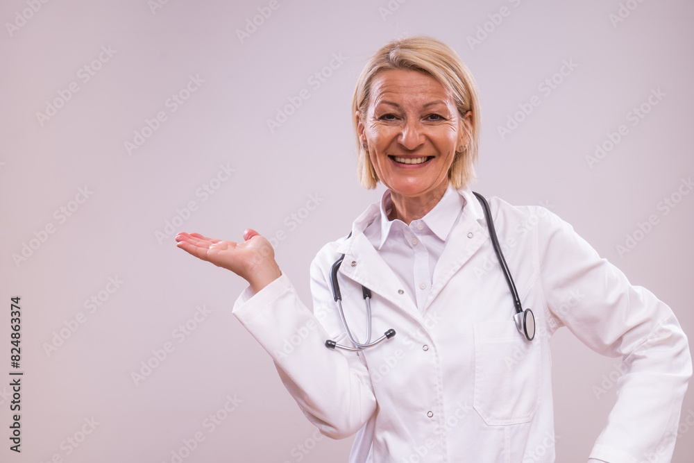 Portrait of mature female doctor showing palm of hand on gray background. Portrait of mature female doctor showing palm of hand on gray background.