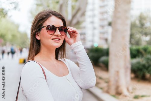 Portrait of a female tourist who is walking in the city, smiling and wearing sunglasses