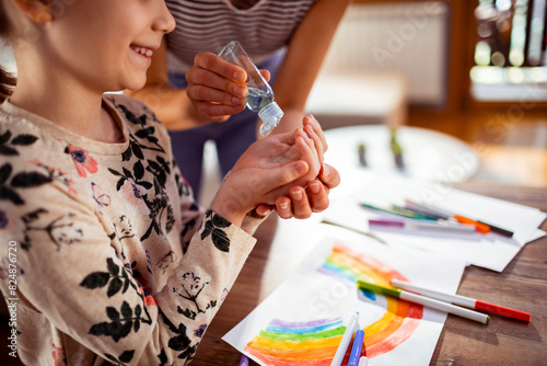 Mother giving daughter hand sanitizer while doing crafts at home photo