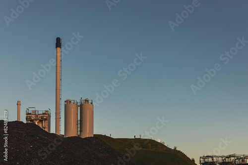 Industrieanlage mit Silos und Schornstein vor einem Hügel bei Abendhimmel in Frankfurt-Griesheim photo