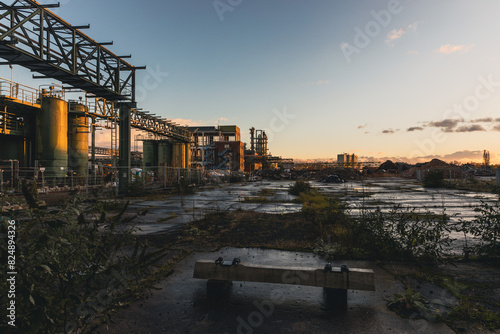Verlassener Industriepark mit Bank im Vordergrund – untergehende Sonne über urbanem Verfall photo