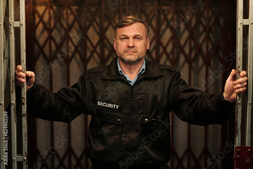 Φωτογραφία Serious security guard in black uniform looking at camera while opening or holdi