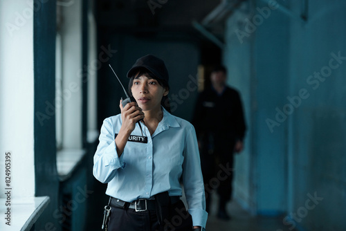 Canvas Print Young female security guard in uniform and cap speaking on walkie-talkie to her
