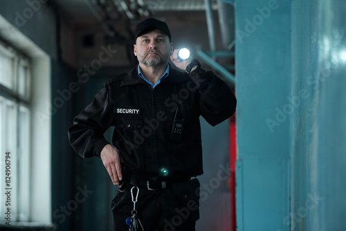 Konstfotografi Mature male security guard in uniform and cap lighting forward with flashlight w