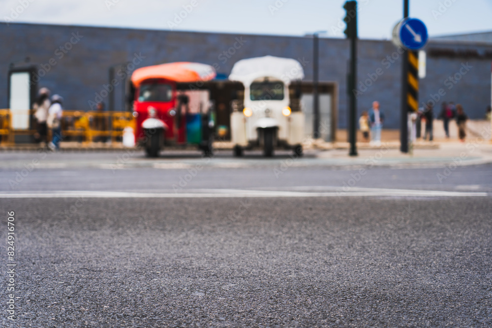 Asphalt road in the city of Lisbon and in the background, out of focus, 2 tuk tuk cars.
