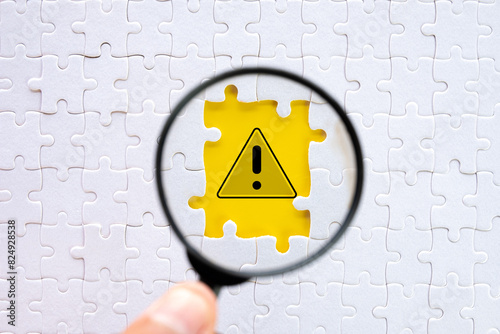 Magnifying Glass Focusing on Exclamation Mark in Breakthrough Yellow Paper Hole Among Puzzle Pieces Sign Highlighting Safety and Hazard Prevention,caution sign, alertness in risky situations.