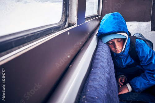 Tired boy wearing blue jacket sleeping in vehicle photo