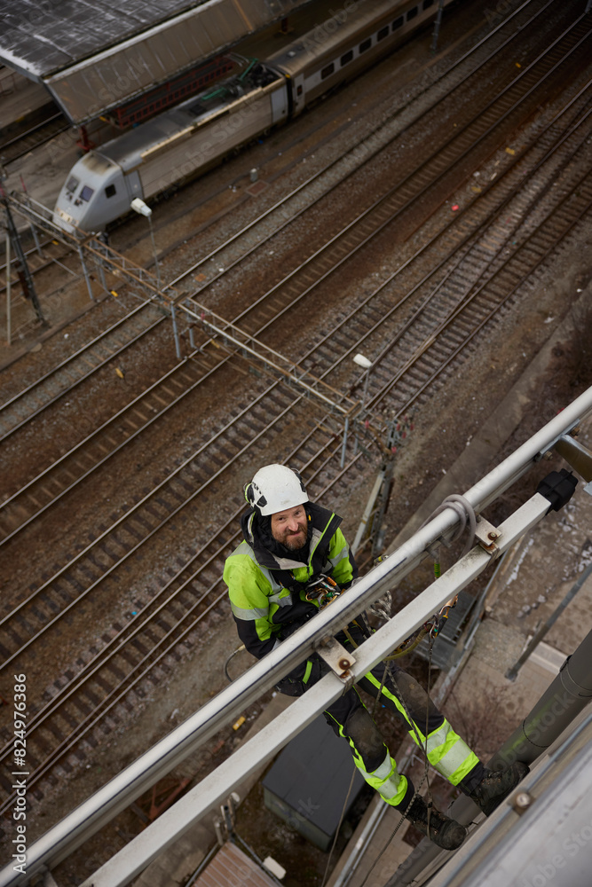 High angle view of rope access worker hanging on building by railroad tracks High angle view of rope access worker hanging on building by railroad tracks