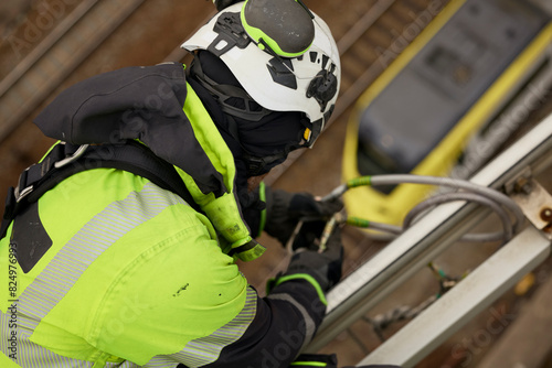 High angle view of male worker in protective workwear attaching carabiner on metal photo