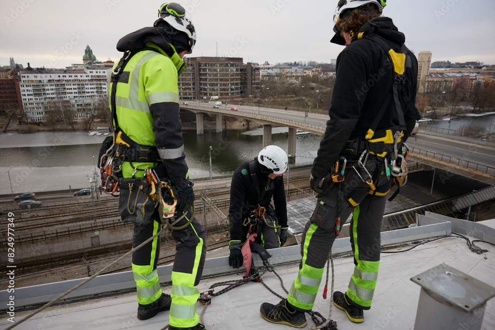 Male rope access workers looking at coworker on rooftop Male rope access workers looking at coworker on rooftop