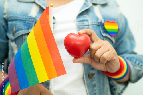 Asian lady wearing rainbow flag wristbands and hold red heart, symbol of LGBT pride month celebrate annual in June social of gay, lesbian, bisexual, transgender, human rights.