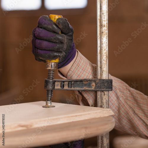 Carpenter's hands wearing safety gloves using screw clamp on wooden furniture