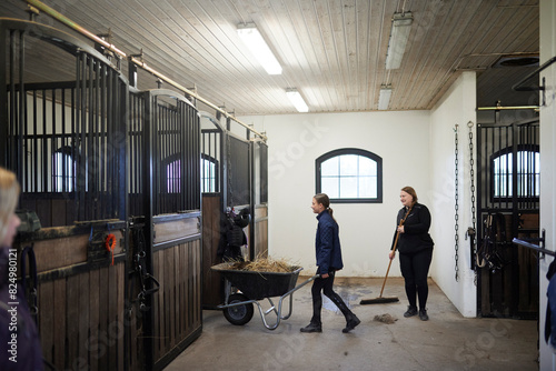 Girl and female farmer cleaning stable together