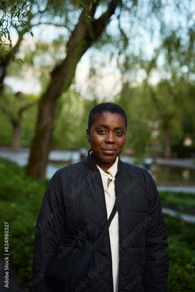 Portrait of woman in black jacket with crossbody bag standing at park Portrait of woman in black jacket with crossbody bag standing at park