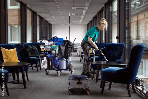 Full length of mature female janitor cleaning lobby with vacuum cleaner photo