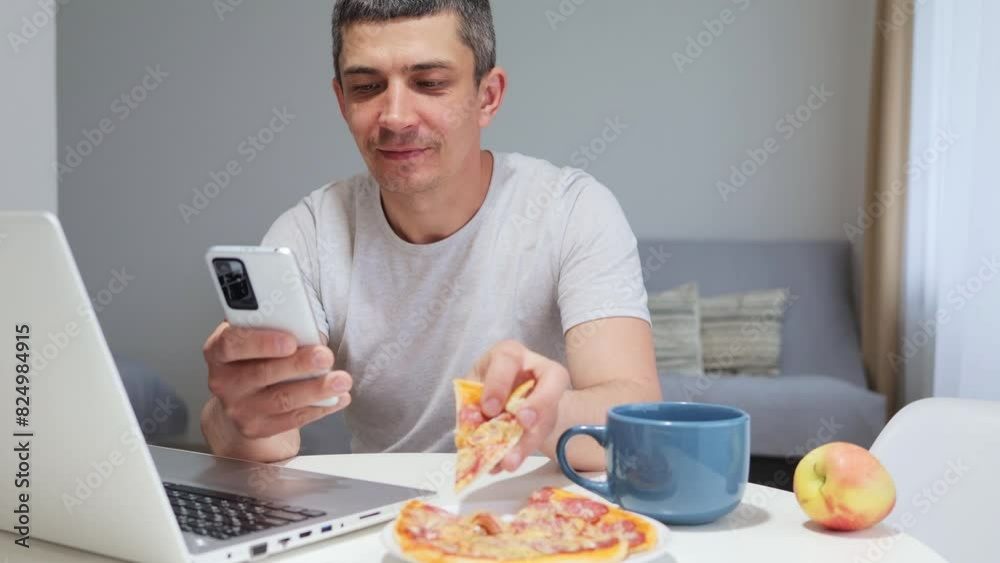 Handsome pleased young man freelancer working on laptop and using smartphone in his home office and eating delivering pizza surfing internet shopping online ordering dessert Handsome pleased young man freelancer working on laptop and using smartphone in his home office and eating delivering pizza surfing internet shopping online ordering dessert