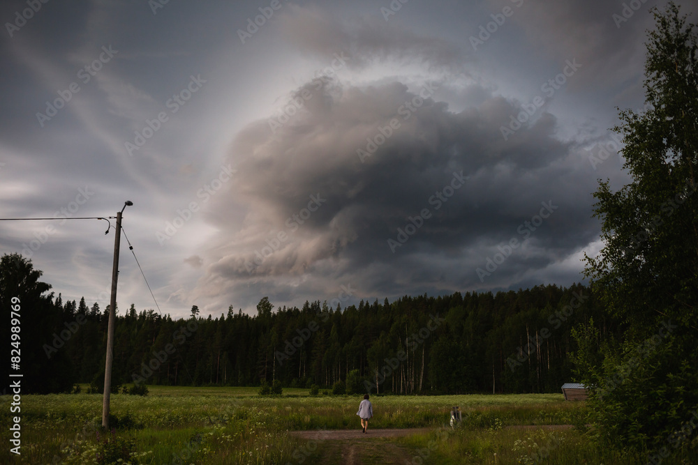 Person walking towards meadow with stormy clouds Person walking towards meadow with stormy clouds
