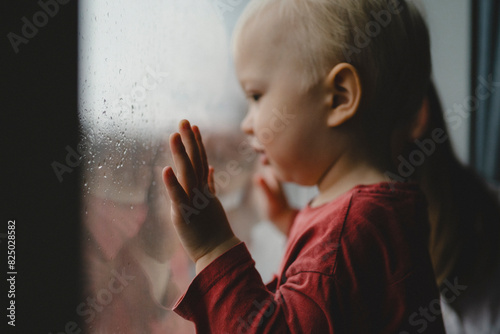 Side view of cute blond boy looking out through from window at home photo