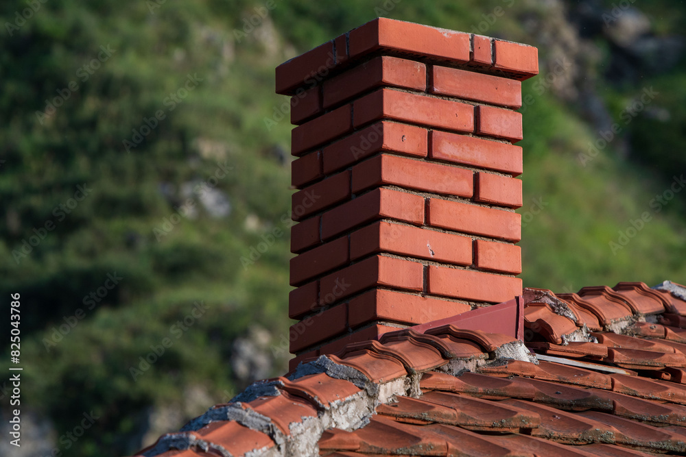 Naklejka premium The Brick Chimney. A Play of Light and Shadow on the Rooftop. Green blurry background.