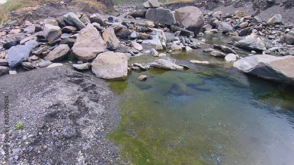 horizontal look up left then right pane view of still water pond pool standing on pile of gravel of riverbed with green moss growing underwater and blue sky in reflection boulders of colorful rocks horizontal look up left then right pane view of still water pond pool standing on pile of gravel of riverbed with green moss growing underwater and blue sky in reflection boulders of colorful rocks